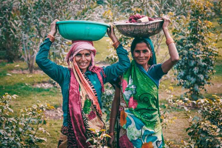 two women wearing traditional dress carrying basins